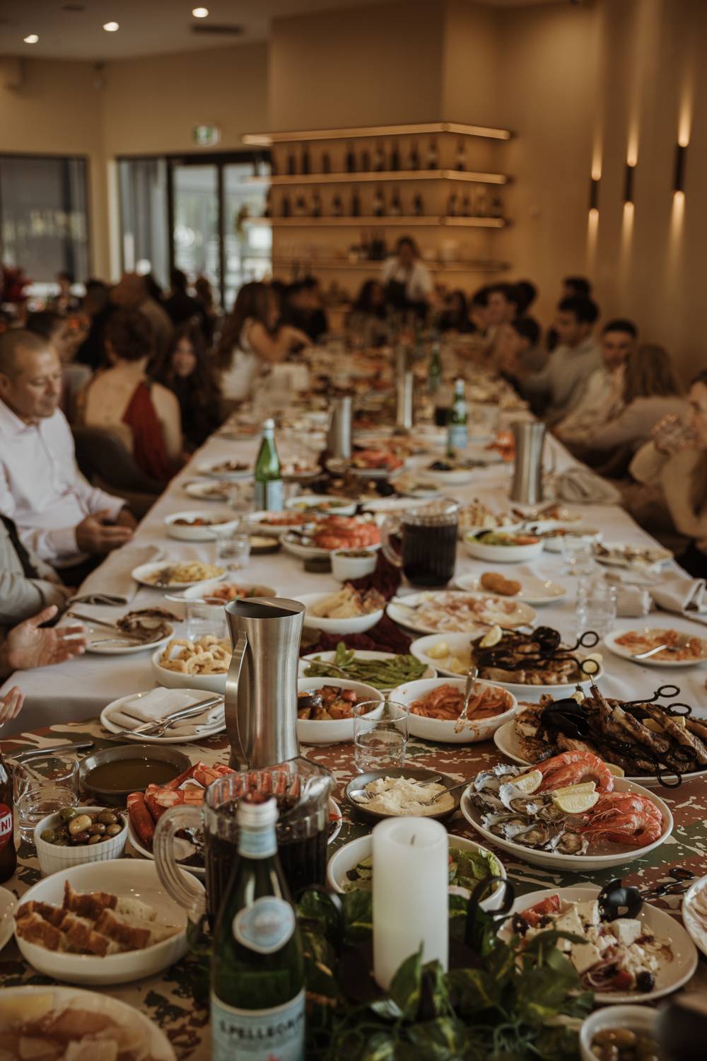 A long shared table filled with seafood, grilled meats and plates to share, with guests dining together