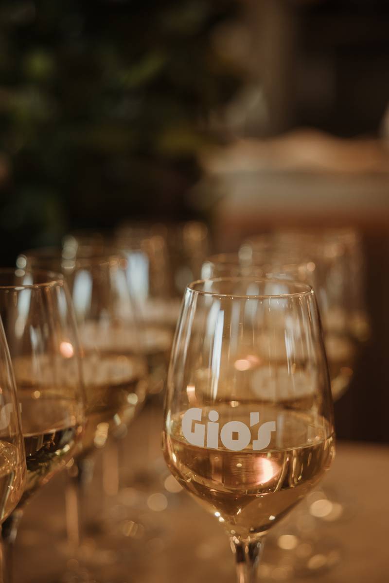 Glasses of white wine, one printed with the Gio's logo