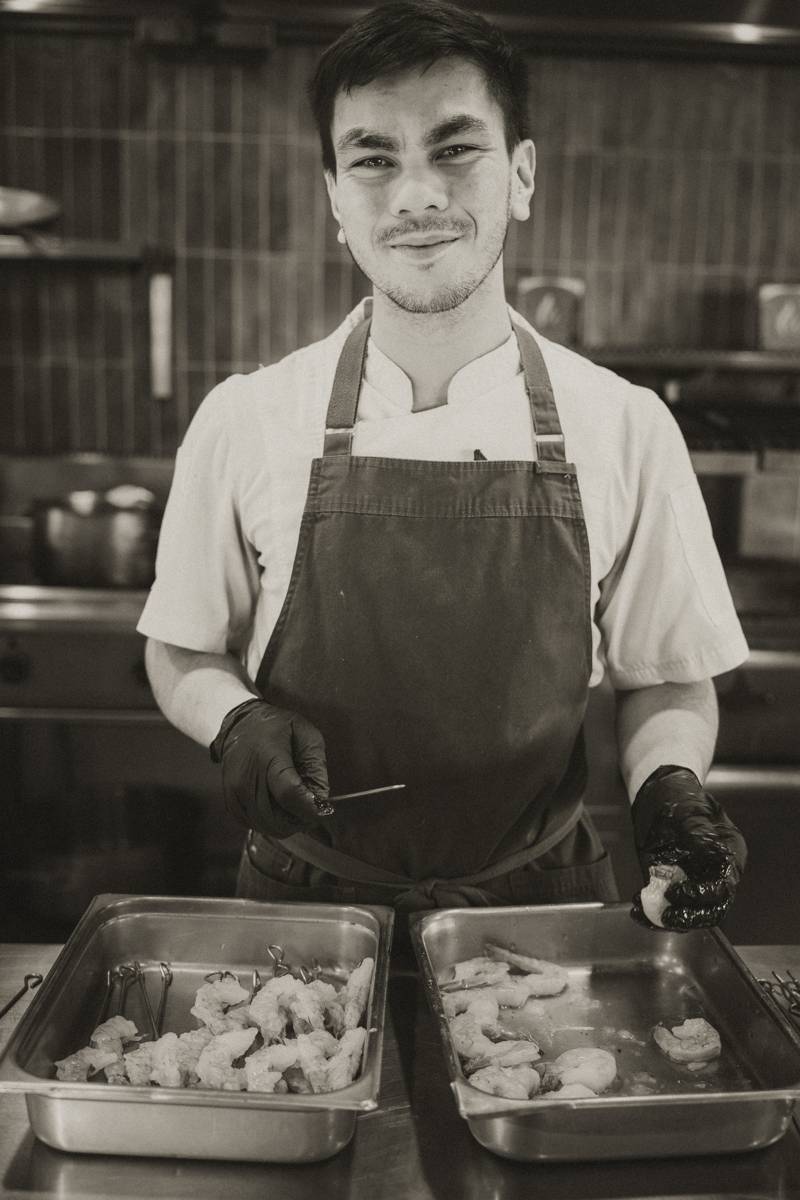 A smiling chef in an apron preparing prawn skewers in the kitchen